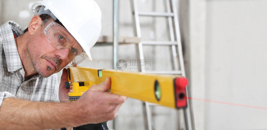 建筑工人在室内建筑工地用水平激光佩戴安全帽和图片