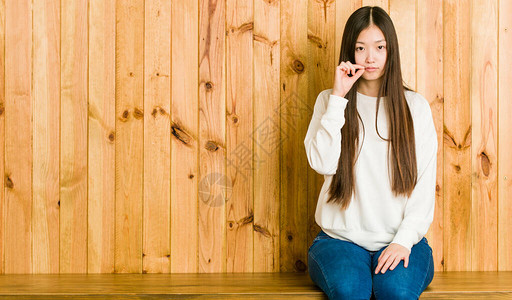 年轻的女人坐在木制地方嘴唇上用手指图片