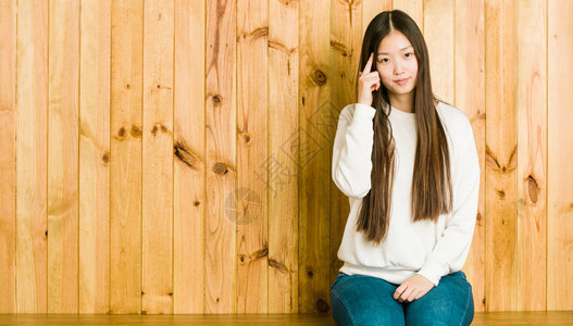 年轻女人坐在木制地方用手指对着思考专图片