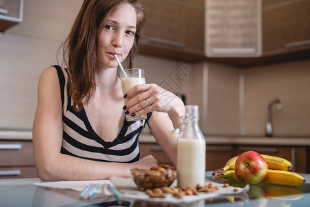 妇女在厨房里用手握着玻璃的有机杏仁奶水饮用图片