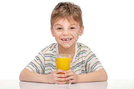 快乐的小男孩的肖像杯橙汁坐在白背景的桌子上图片