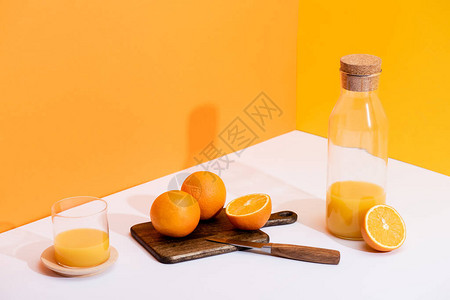 玻璃瓶中的新鲜橙汁和靠近成熟橙子的瓶子在切板上图片