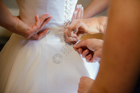 伴娘帮修长的新娘系上白色婚纱图片