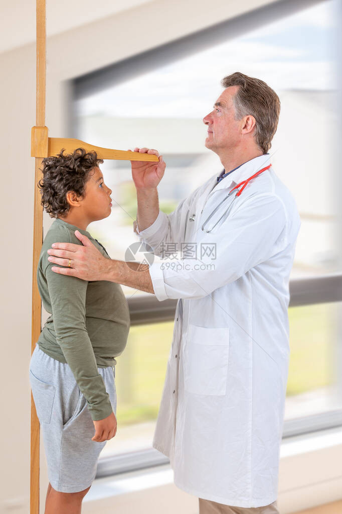 医生测量男青少年在体格检查期间的身高图片