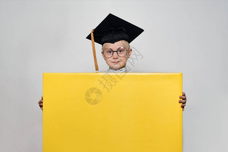 身戴学术帽子和眼镜的金发男孩拿着一个大盒子图片