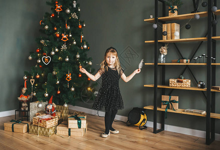 一个身着黑色裙子手握小羽毛的小女孩站在圣诞树附近的喜图片