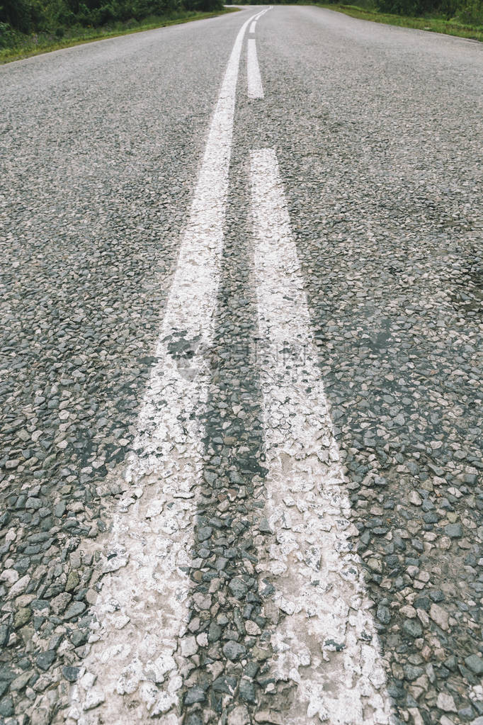 微小的沥青砾石公路关闭颗粒状石头粗糙柏油路的背景与透视的白色道路标记详细的垃圾纹理与散景有复制空图片