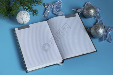 灰色笔记本被银闪发光的圣诞装饰环绕在蓝色背景上图片