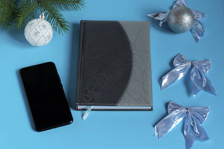 灰纸笔记本和黑电话周围是银色闪的圣诞装饰蓝色背图片