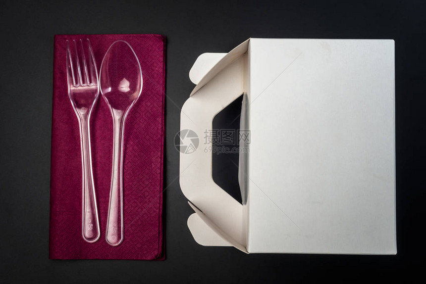 白色纸板快餐盒午餐包装和紫色餐巾纸上的塑料叉子和勺子在被隔绝的黑色背景上准备好图片