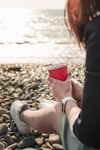 女孩坐在沙滩上时手里拿着红杯咖啡图片