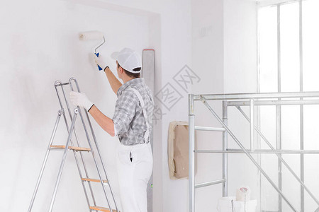 站在梯子上的画家在正施工的房间里画白墙图片
