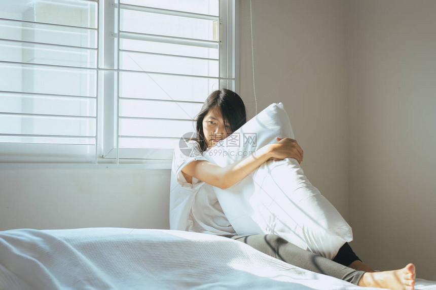 亚裔女人早上醒来后有深思熟虑的拥抱枕头在图片