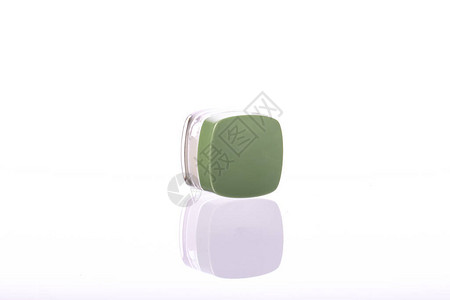 带绿色盖子的化妆品奶油罐位于其侧面图片