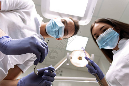 牙医和助手弯腰检查患者的牙齿治疗牙齿或制作假牙一男女拿着检查仪器唾图片