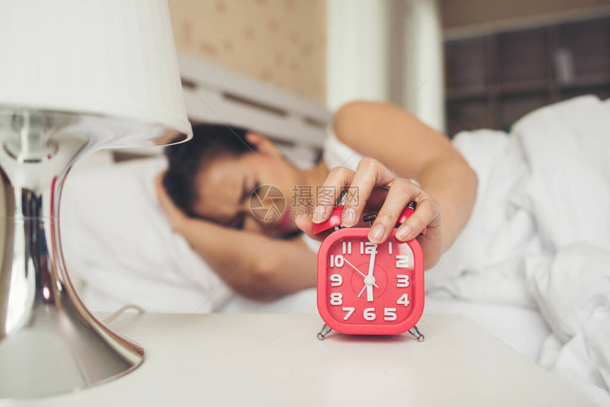 懒女人手拿着闹钟在床上图片