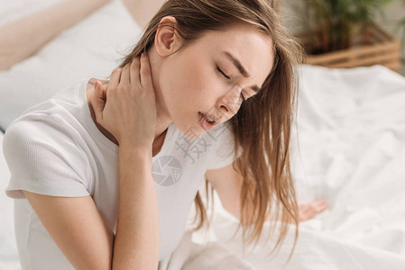 女青年闭着眼睛坐在床上颈部疼痛图片