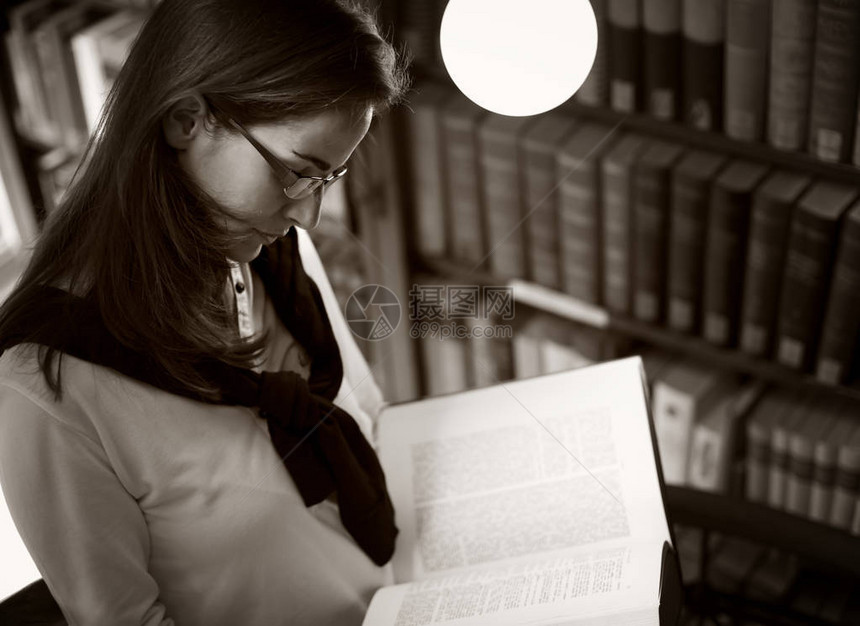 学生在旧大学图书馆的书架上站立着戴眼镜的学生正在阅读一本书图片
