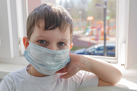 一个戴着医用口罩的可爱悲伤的四岁男孩坐在阳台上图片