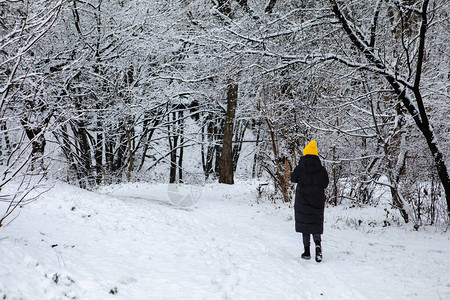 身穿黑冬衣和黄帽子的妇女经雪地城市公园图片