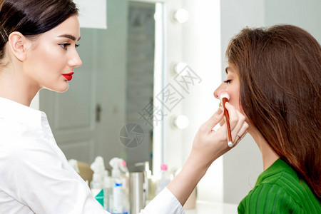 专业化妆师在美容院为年轻漂亮的女人在脸颊图片