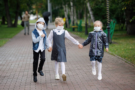 在校儿童一名戴医疗面具的男女学生在市公园散步图片