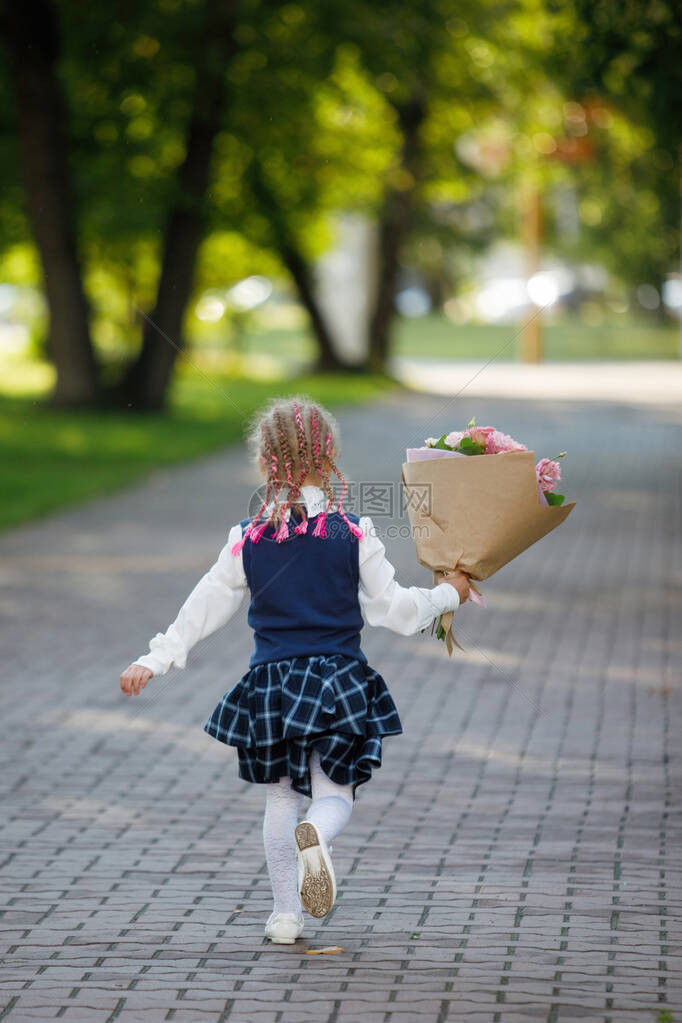 学年开始时拿着一束鲜花的女学生穿着制服沿着城市公园的人行道散步第一次上第一图片