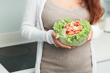 怀孕的年轻孕妇用生菜和番茄配着一碗美味健康沙图片