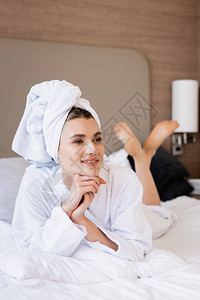 穿着毛巾和白浴袍的赤脚妇女躺在床上在图片