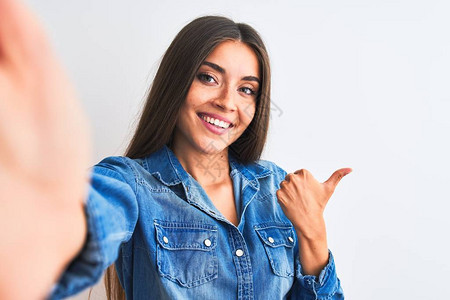 穿戴迪尼姆衬衫的漂亮女人用相机拍着独白背景的自拍指向后背手和拇指举起图片