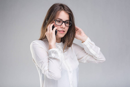 戴眼镜的微笑女商人谈手机美丽的年轻女孩在白色孤立的背景上谈手机的白衬衫穿衬衫的女人拿着手机复制背景图片
