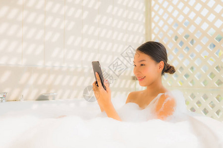 在浴缸使用智能手机进行SPA概念的肖像年图片