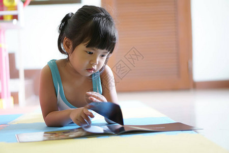 亚洲儿童可爱或小女孩躺着学习阅读故事书或故事和卡通在地板上背景图片