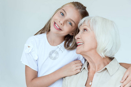 微笑着的孙女拥抱着祖母看着在灰色上图片