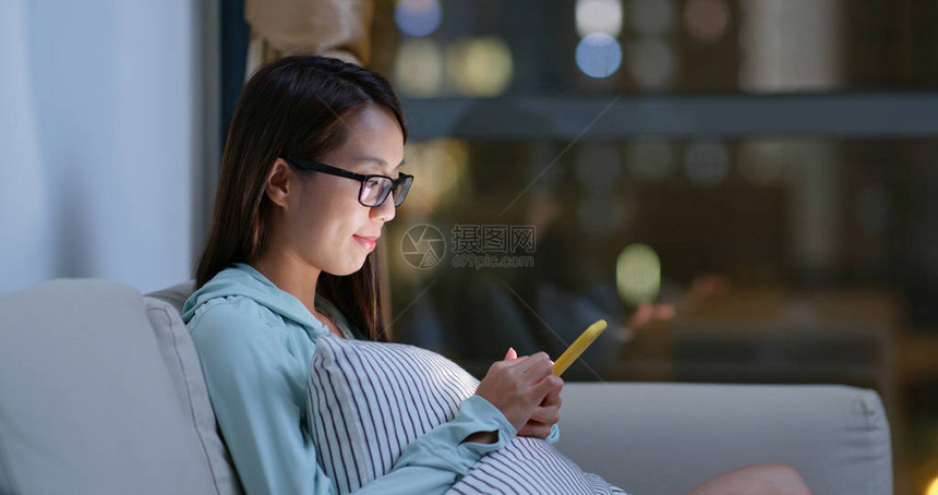 晚上在家戴眼镜并使用移动电话的女图片