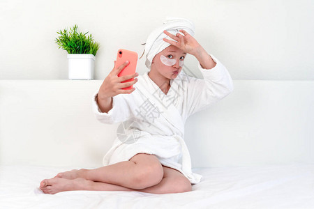 一位十几岁的女孩博主穿着白色浴袍坐在床上背景图片