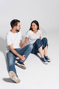 穿着白色T恤衫牛仔裤和口香糖的年轻异族青年夫妇坐在白图片