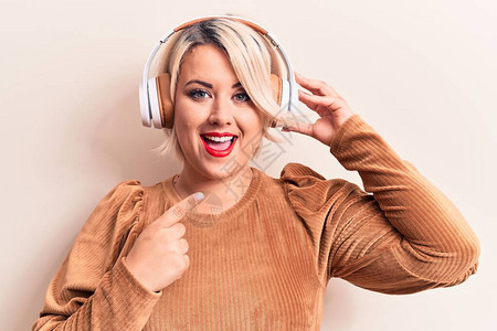 金发碧眼身材魁梧的女人用耳机在白色背景上听音乐图片