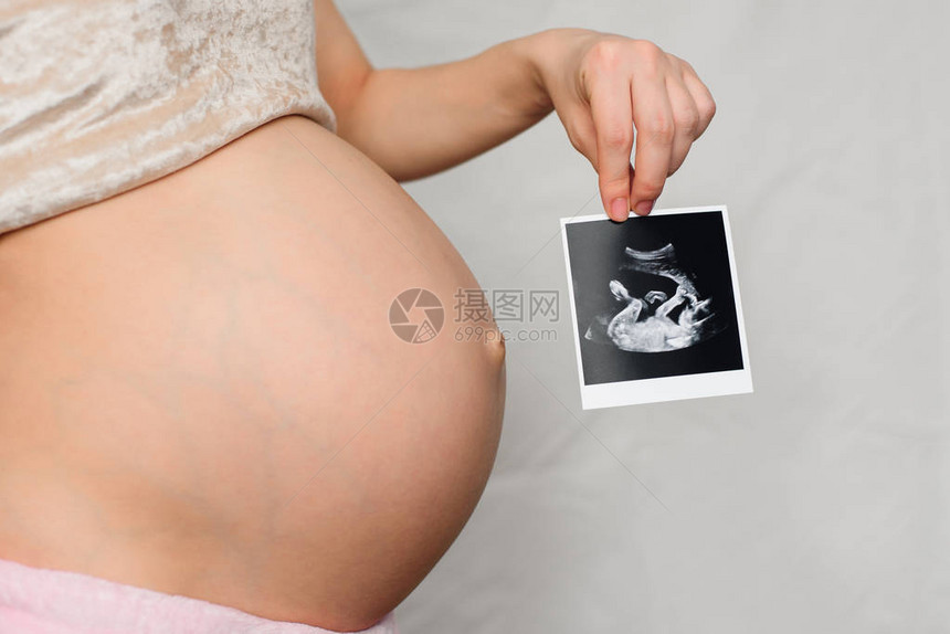 孕妇腹部背景下怀孕女孩手上的孕妇超声波照片图片