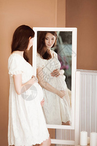 身着白裙子的美丽怀孕的黑发美女图片
