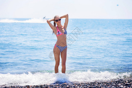 一个穿着条纹泳衣的漂亮的苗条女孩和太阳镜在度假时站在海图片