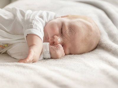 产褥期美丽的新生男孩的肖像正在睡觉他的双臂交叉在背景