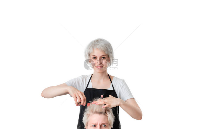相当年轻的理发师白色T恤和黑色围裙将头发剪成短发的金发女郎孤立在白色背景客户如果对图片