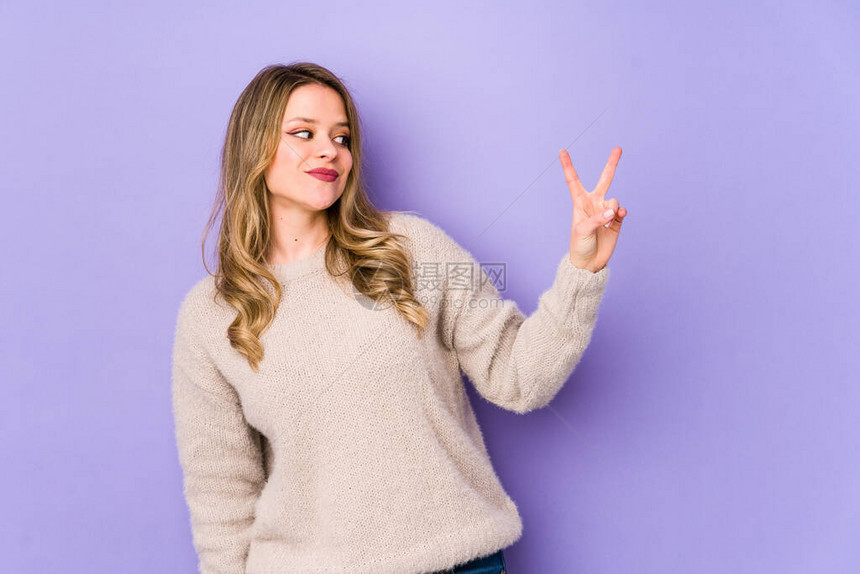 在紫色背景上被孤立的年轻caucasian女欢乐和无忧虑地展示一个和平图片
