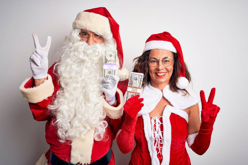 身穿圣诞老人服装的老夫妇拿着美元在孤立的白色背景上微笑着图片