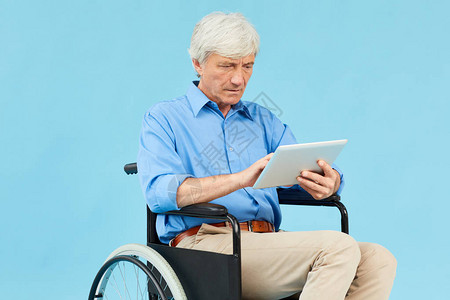 坐在轮椅上并在蓝色背景下使用数字平板片的成年残疾背景图片