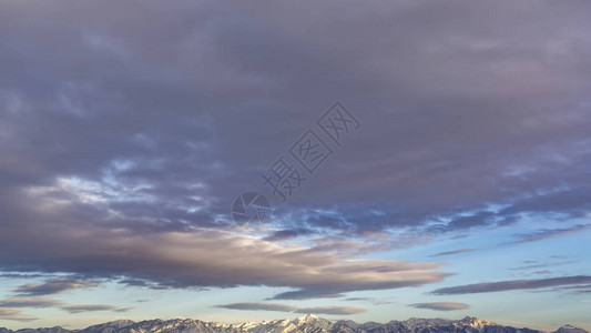 全景雄伟山脉的全景覆盖着锋利的白雪淡蓝色的天空几乎充满了厚的灰色云层背景图片