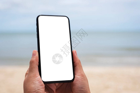 海边用空白桌面屏幕拍摄手持黑色手机的模拟图像空图片