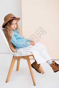 穿着棕色帽子和靴子白裙子和蓝毛衣的时装金发美女坐在米格墙图片