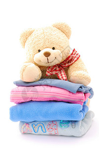 一只可爱的小泰迪熊在看一堆多彩孩子的衣服图像被孤立在白色背景图片